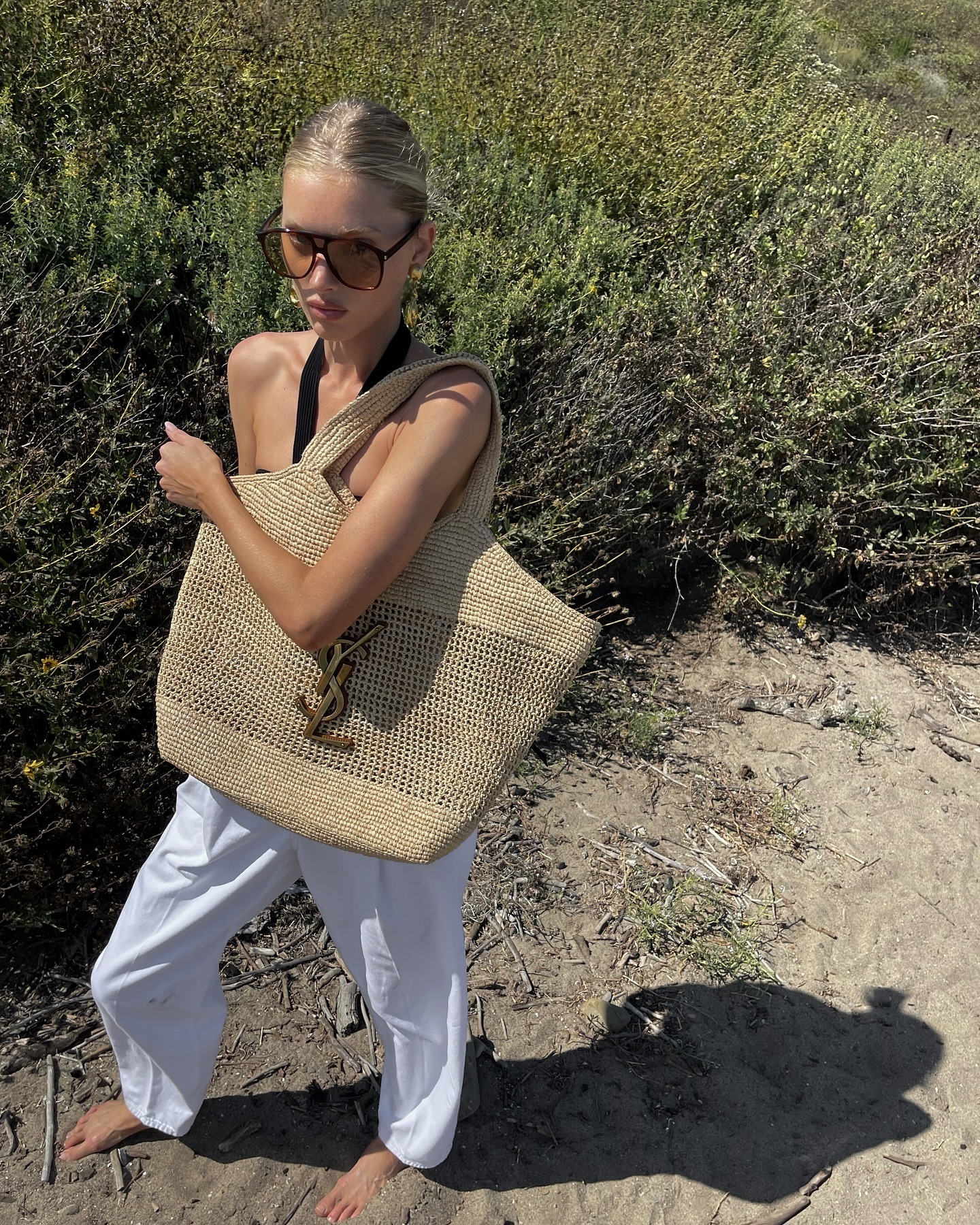 Elsa Hosk wears a black halterneck top, white trousers and carries Saint Laurent iCare in raffia