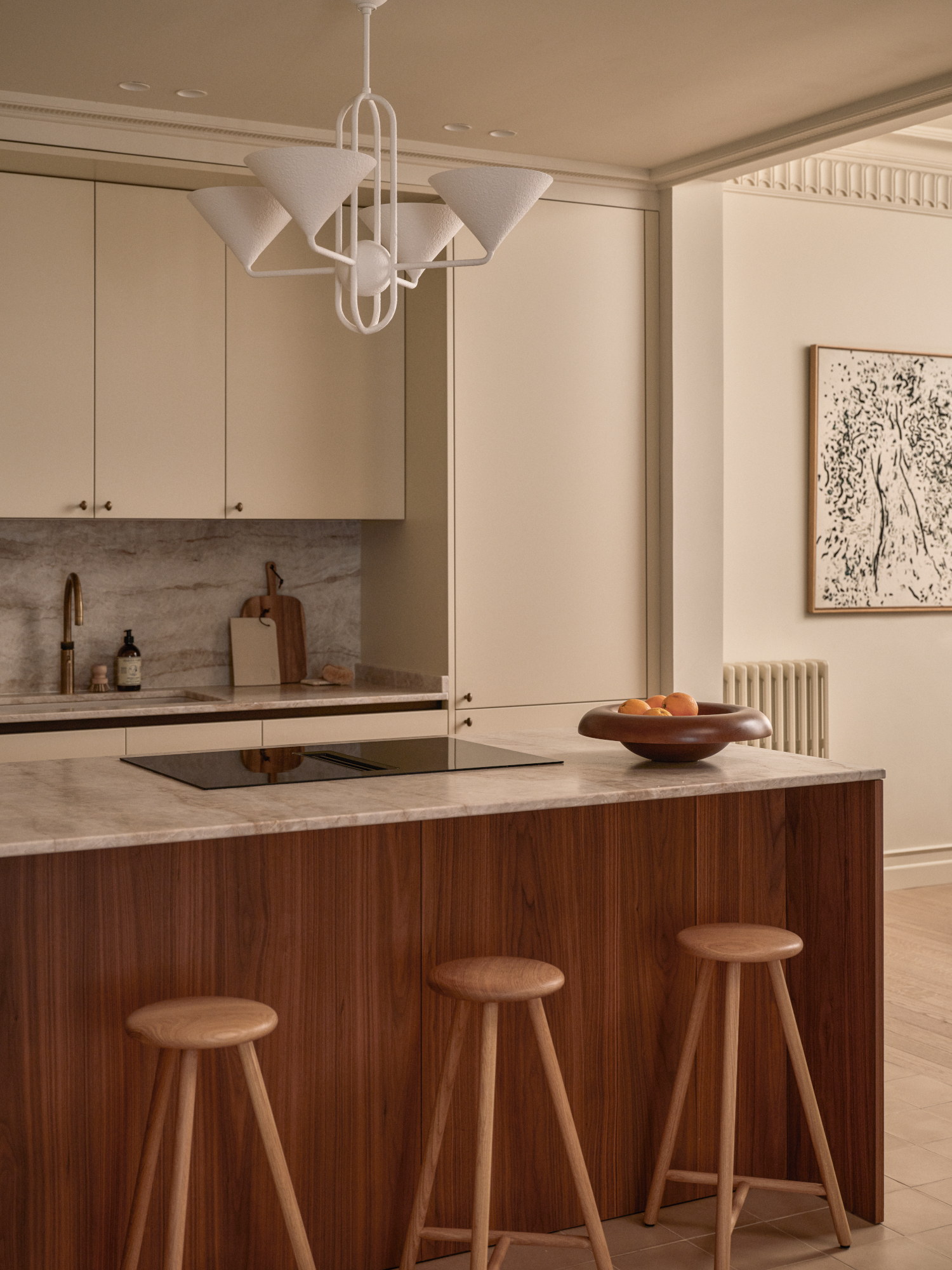 Kitchen with warm white units and wood island, topped with beige marble and with wooden rounded bar stools