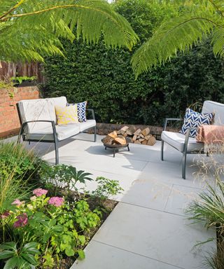 A small paved patio area with two seater sofa and armchair as well as small firepit