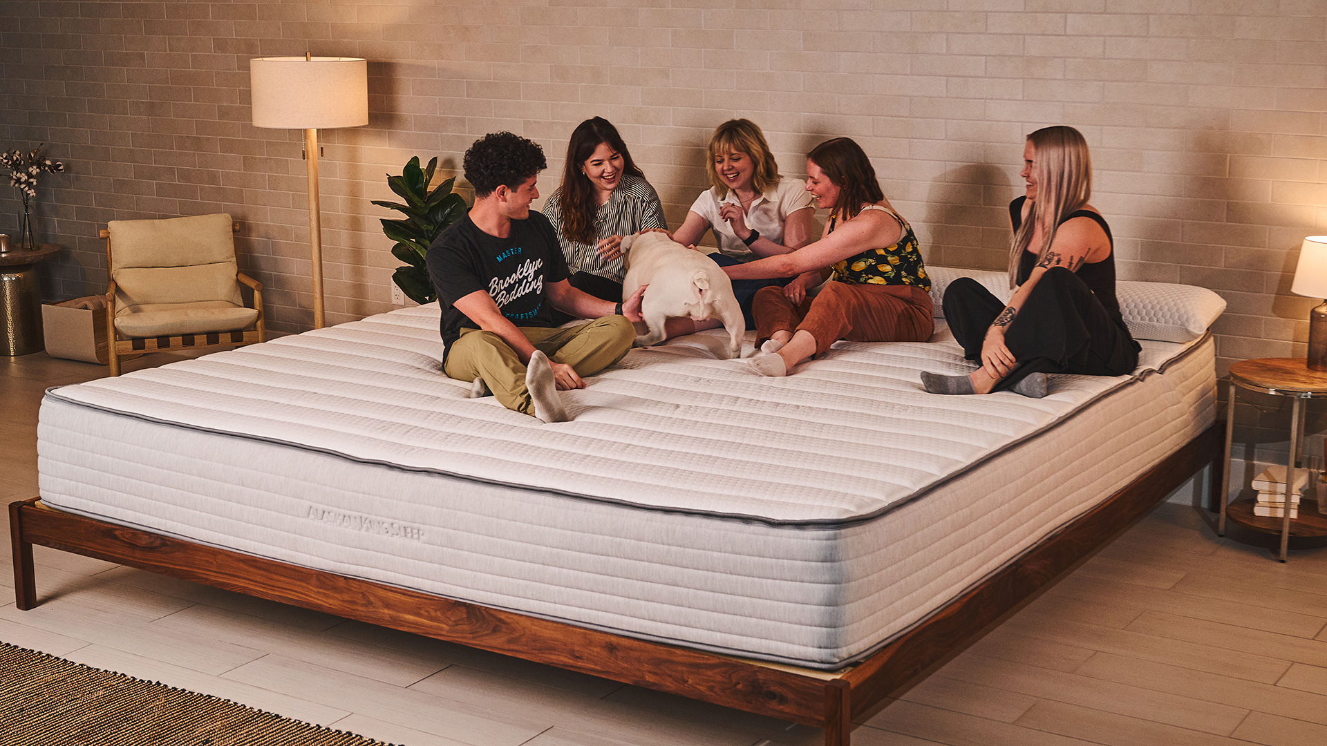 Five testers and a dog sit on the Nolah Luxe Alaskan king mattress, showing how much space there is for families