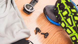 Running shoes, a running watch, a pair of earbuds and a T-shirt on a wooden floor