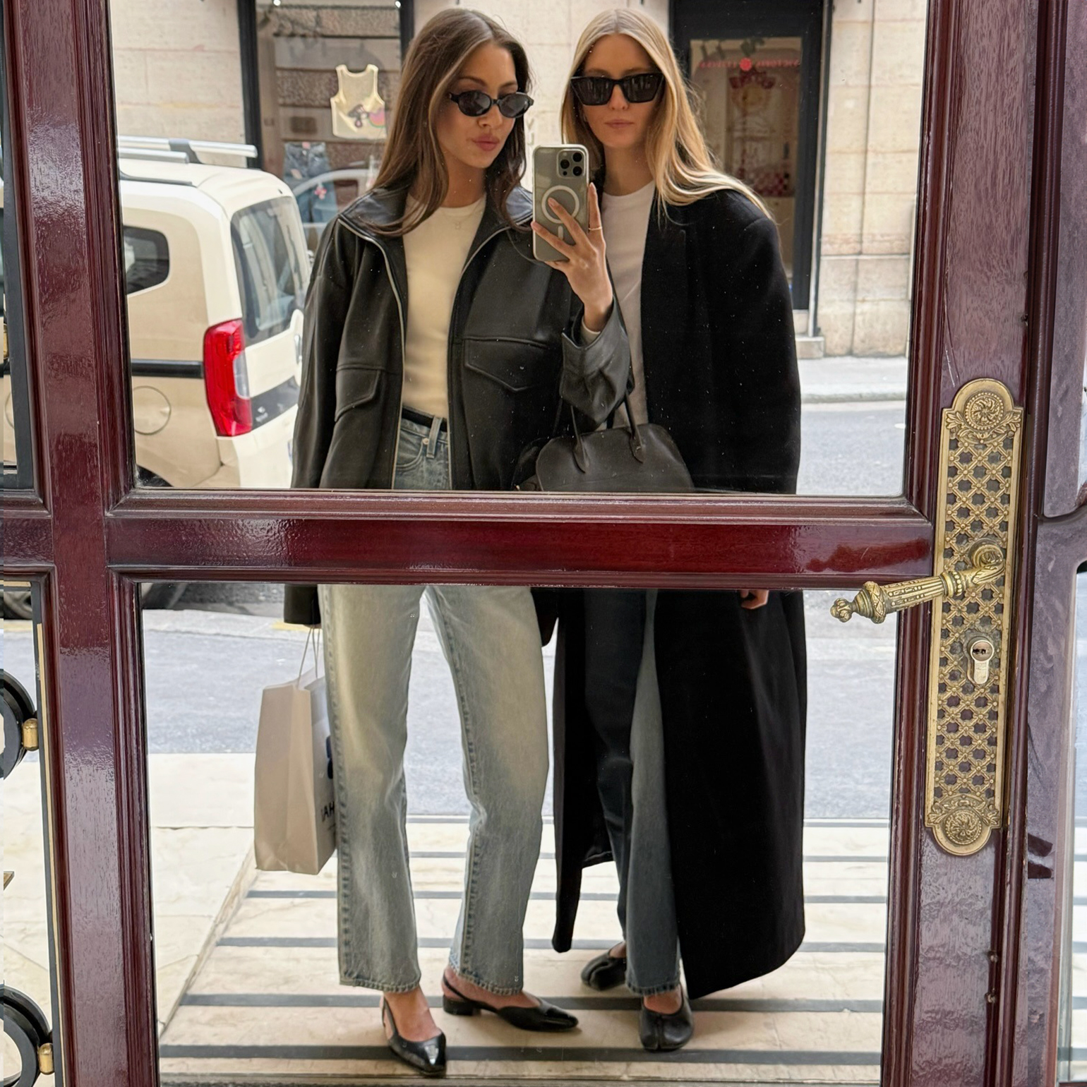 style influencer Felicia Akerstrom and a friend pose for a mirror selfie in Paris wearing black sunglasses, a black jacket and coat, white T-shirts, straight leg jeans and black flats