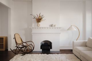 Simple living room with white walls, fireplace, white carpet, and wooden rocking chair