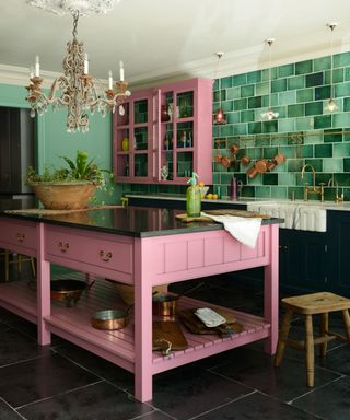kitchen renovation rules, pink and green kitchen with pink island and wall cabinet, shades of green backsplash tiles, brass hanging rail, dark grey floor tiles