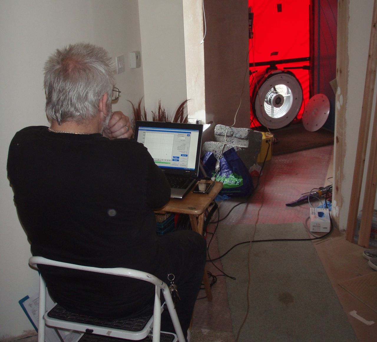 An air tightness test shows a man sitting at a computer whilst a fan connected to a door measures the level of air tightness