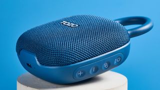 Tozo PE1 speaker in blue with built-in clip photographed on a blue background.