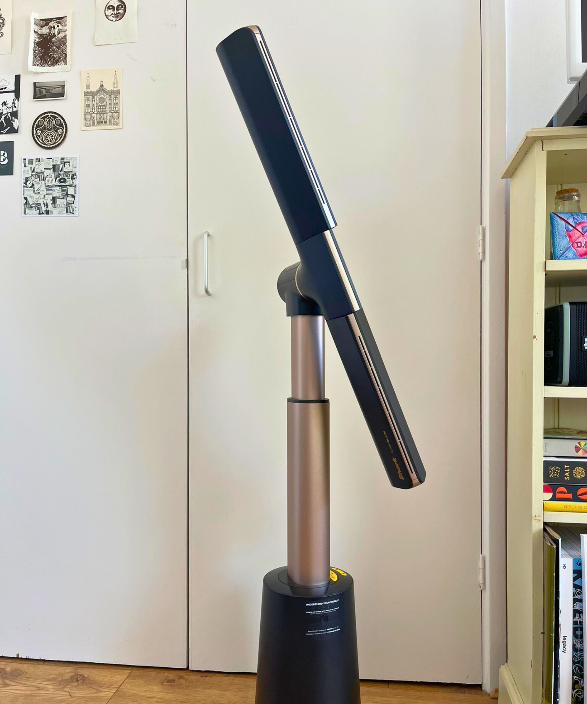 Shark TurboBlade in Dan Fauzi's home in front of white doors with black-and-white prints, next to partially pictured cream bookshelf with books and magazines.