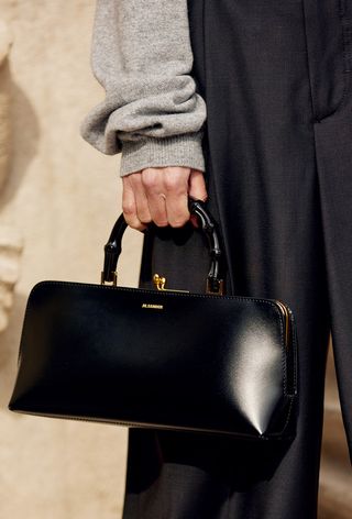 a close up photo of a woman holding a jil sander bag from a luxury resell site