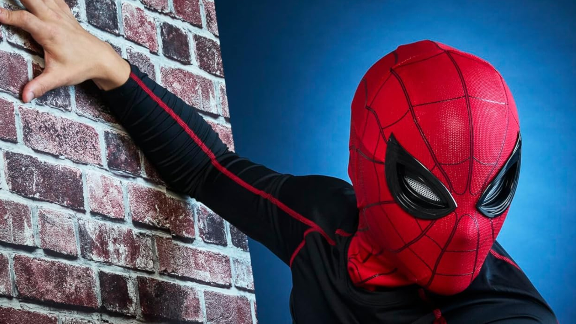 A person wearing a Spider-Man mask grips a brick wall