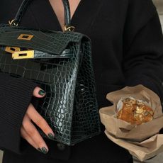 A woman wearing one of the biggest January nail trends, a green refined manicure, created by Julia Diogo, while holding a green Hermès Kelly bag and a muffin