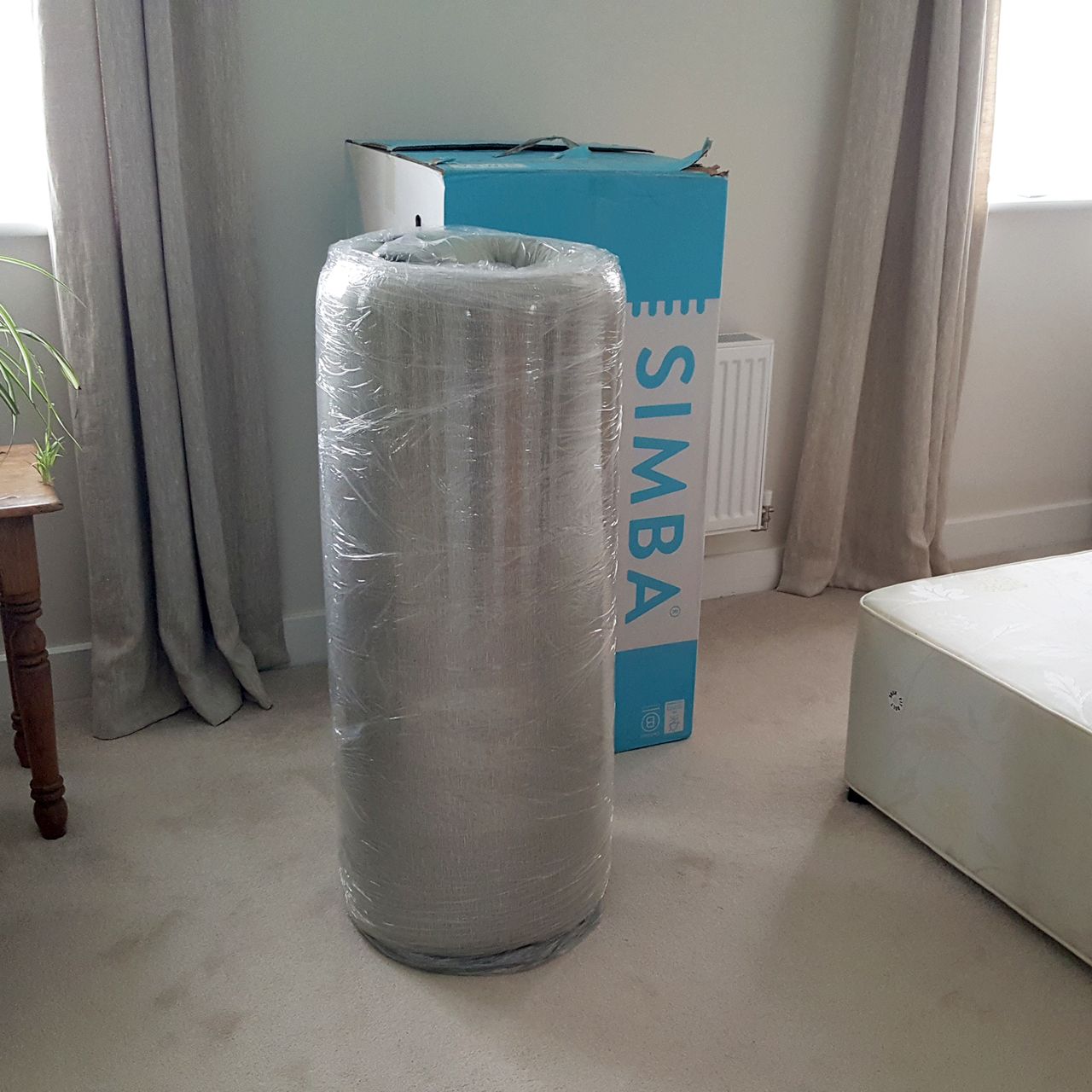 The Simba Hybrid Original mattress rolled up in a bedroom with its packaging box behind