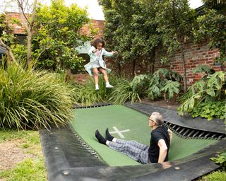 man and child bouncing on an inground trampoline in a garden
