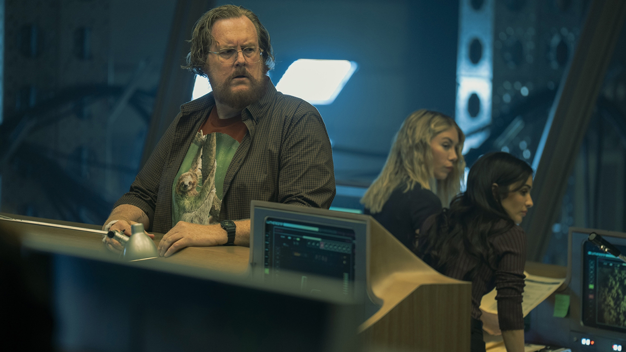 John Economos standing at ARGUS HQ with Emilia Harcourt and Sasha Bordeaux in the background in Peacemaker season 2 episode 8