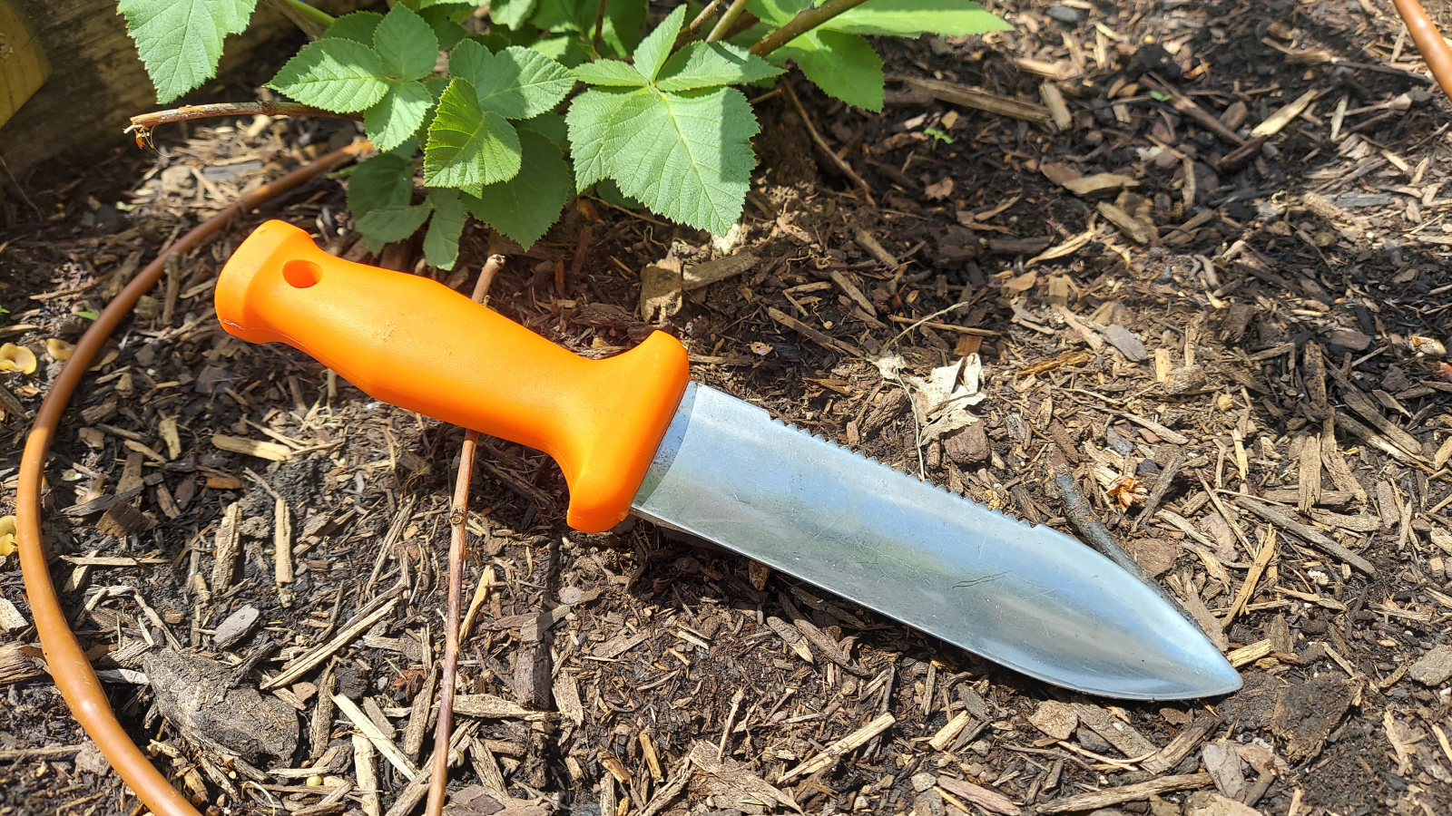 Soil knife with bright orange handle sits in garden bed