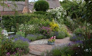 a floral cottage garden with lots of colorful plants in it and a patio in the middle
