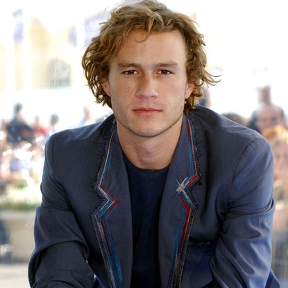 Julia Stiles has blonde hair and wears a white shirt, and Heath Ledger wears a blue blazer and has wavy brown blond hair