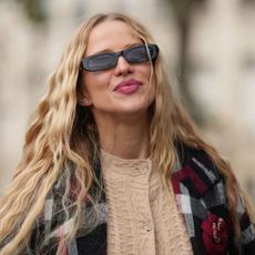 Woman with long blonde, wavy hair walks down the road during fashion week in a tartan jacke t