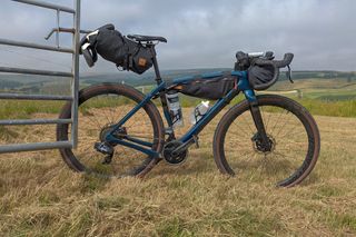 Trek checkpoint sl 7 side on with bike packing bags proped up against gate in field