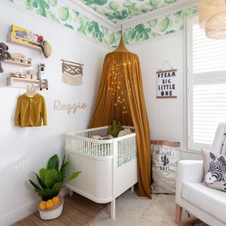 nursery with botanical print wallpaper on ceiling and mustard yellow bed canopy
