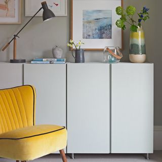 A living room with minimalist grey cabinets and a yellow velvet accent chair