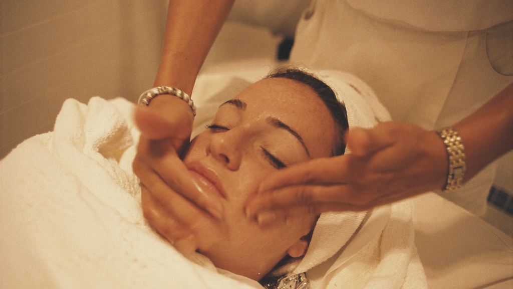 woman with a towel turban lying on a table receiving a face massage