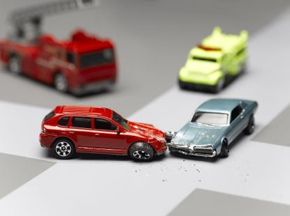 An intersection with four matchbox cars. A red and a blue car had an accident.
