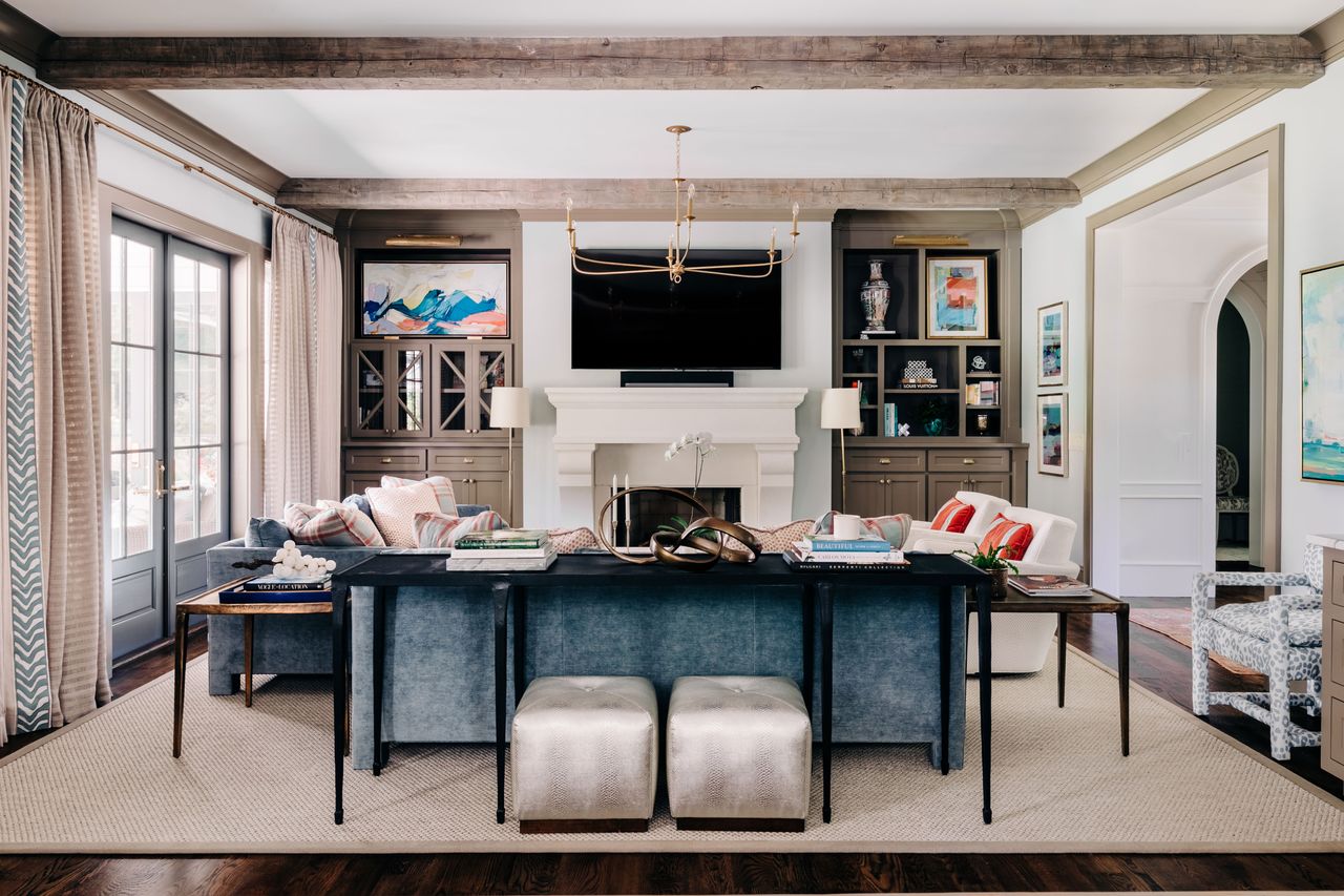 living room with stone fireplace and blue sofas with bright and plaid cushions ceiling beams and modern brass chandelier light
