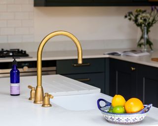 A brass faucet and blue fruit bowl on a white stone countertop.