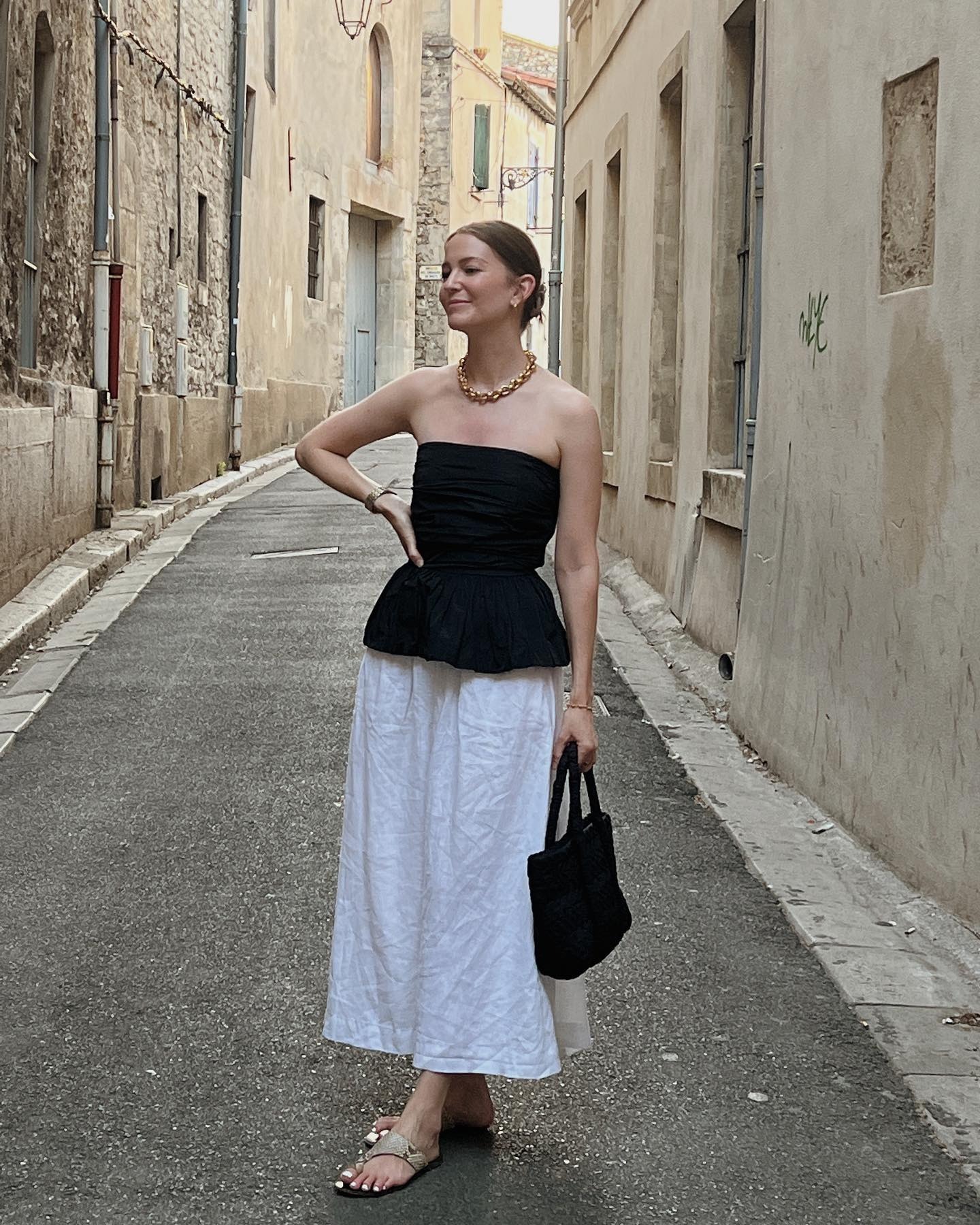 French woman wearing a white maxi skirt, black tube top and snakeskin sandals.