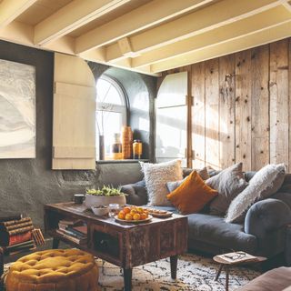 A living room with exposed wooden panelling on the walls, a reclaimed wood coffee table and various cushions on a low sofa