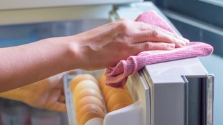 woman wiping fridge door with a pink cloth