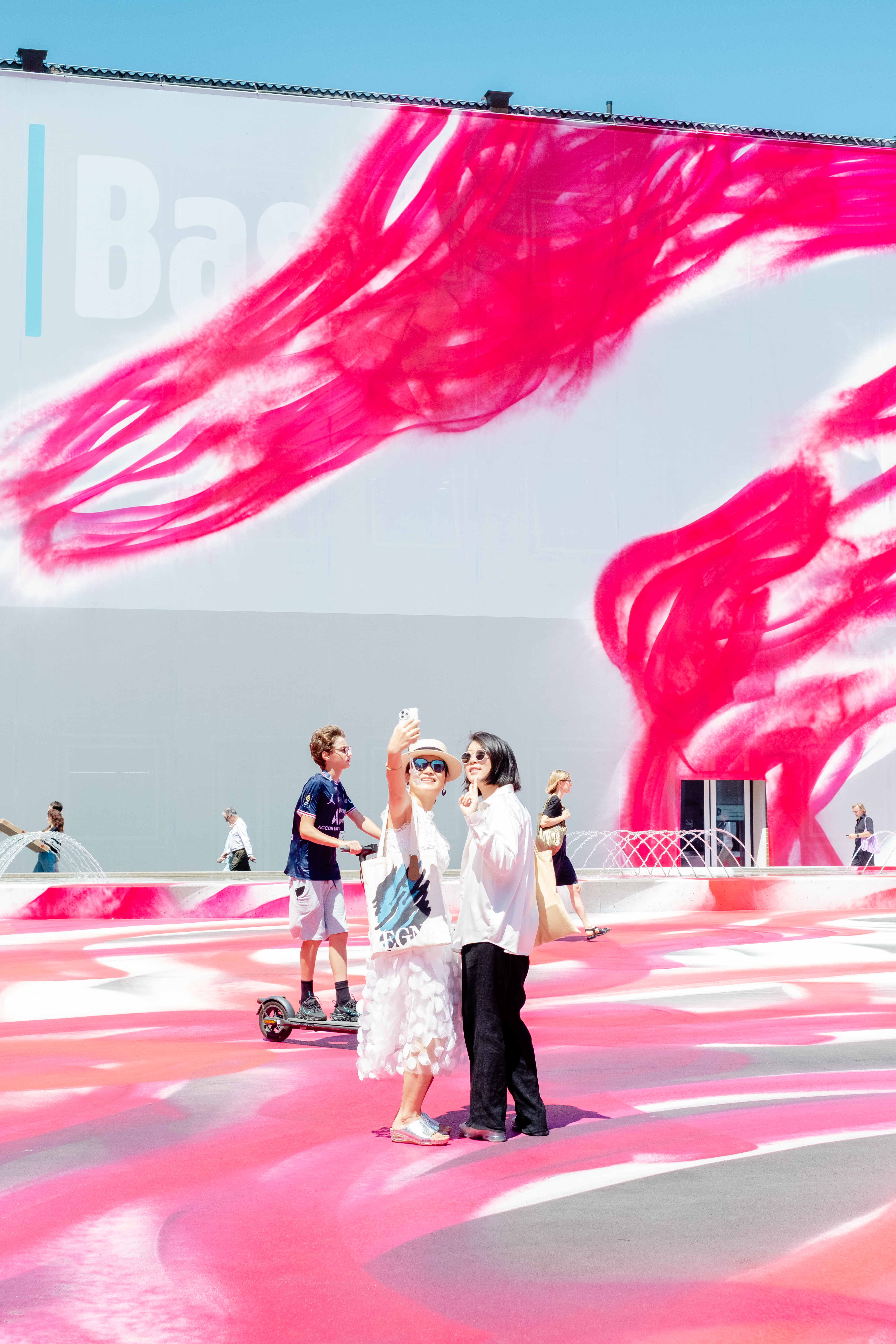 A series of lifestyle images depict people at leisure and play in a Swiss town bathing in sunshine, whether enjoying the weather near the river bank or abstract painting murals at an art fair.
