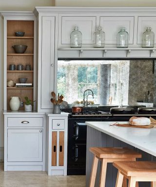 A country style kitchen with a black range cooker below a mirrored backsplash and light gray cabinets