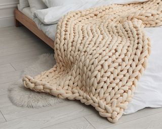 Neutral chunky knitted blanket on bed on low slung wooden bed with white bedding