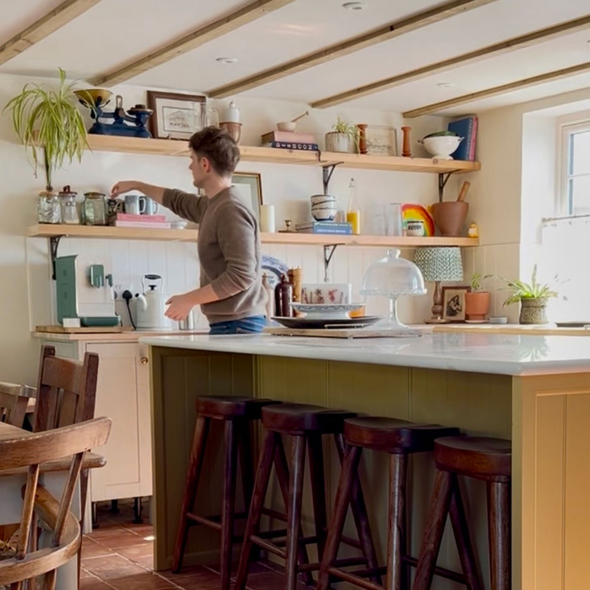 Man putting item onto open shelving in kitchen with island