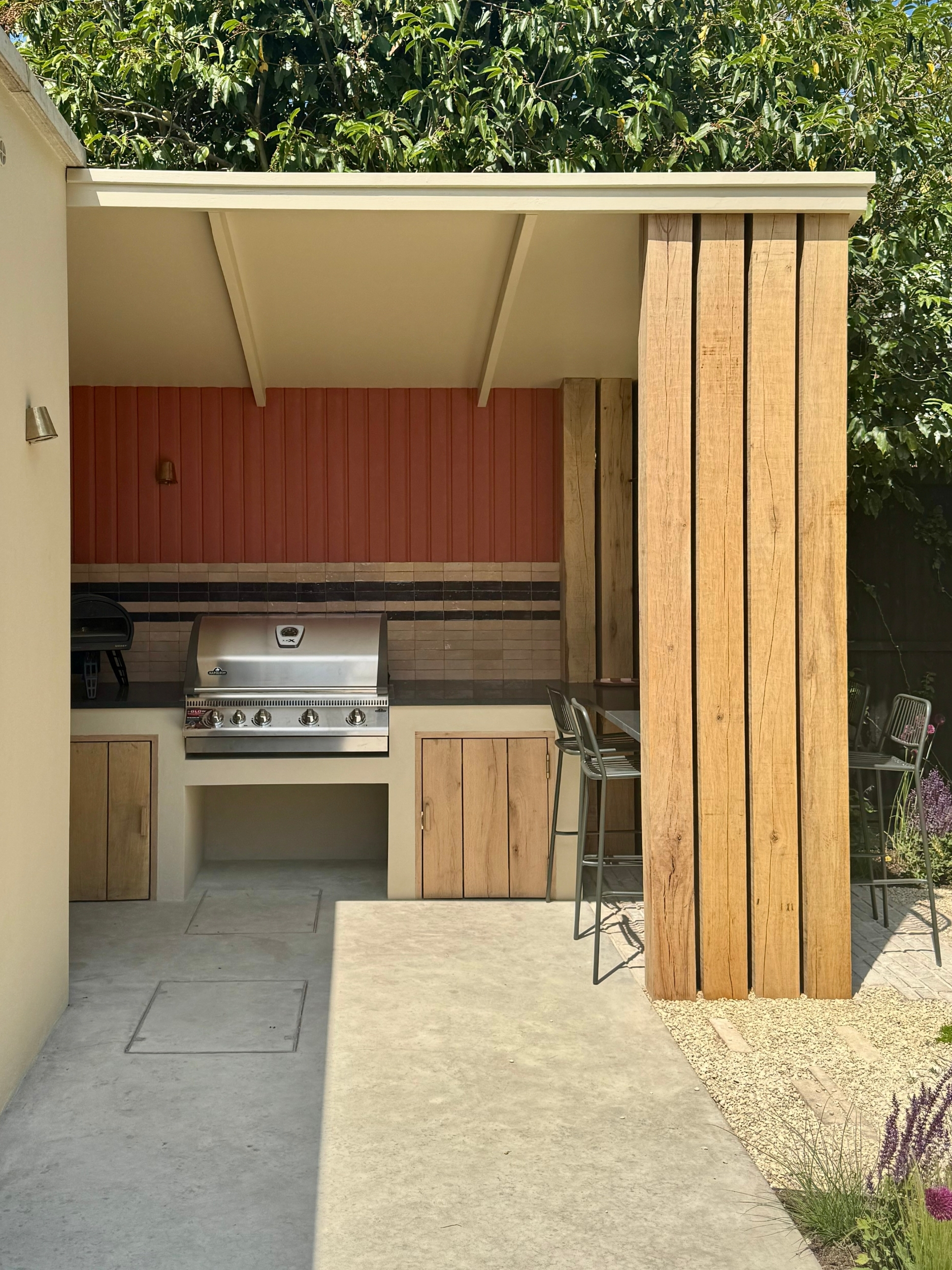 an outdoor kitchen with timber finishes, and a red painted outdoor wall, with a large grill