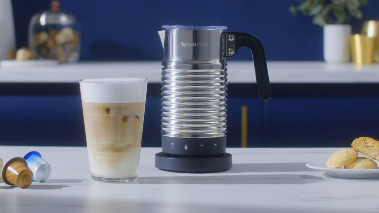 Nespresso Aeroccino 4 on a countertop with a latte,coffee pods, and biscuits on the countertop