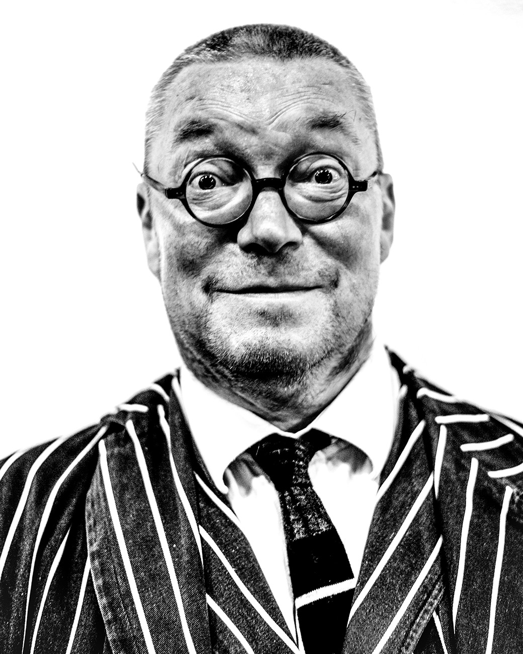 A man in a black and white striped suit with a tie, standing against a plain white background