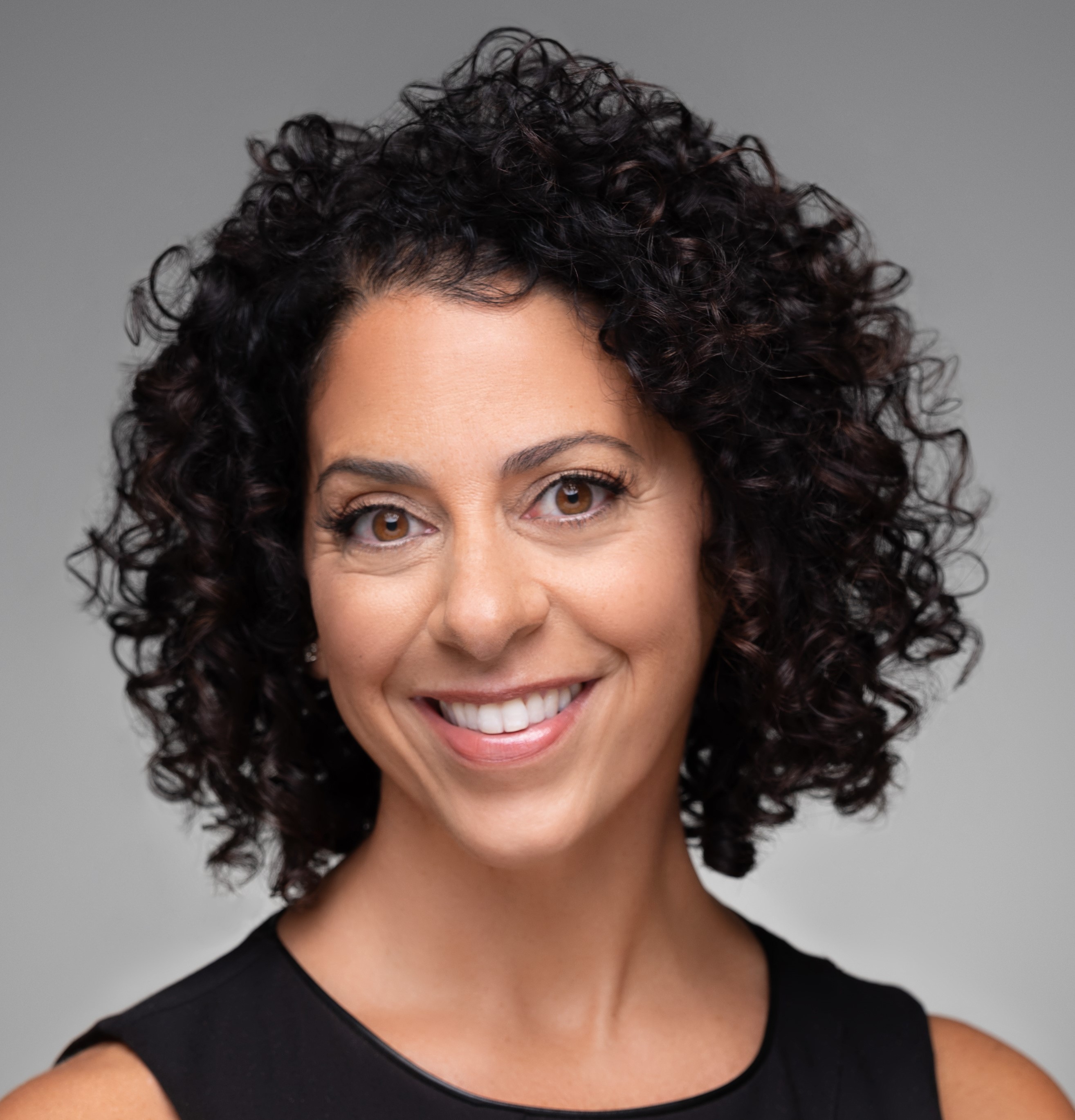 A headshot of a woman with curly dark hair smiling at the camera