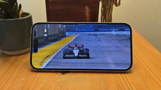 Apple iPhone 16 smartphone on wooden table with F1 car on screen