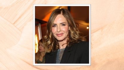 Image of Trinny Woodall smiling with curling brunette shoulder-length hair and wearing a black blazer, on a peach background