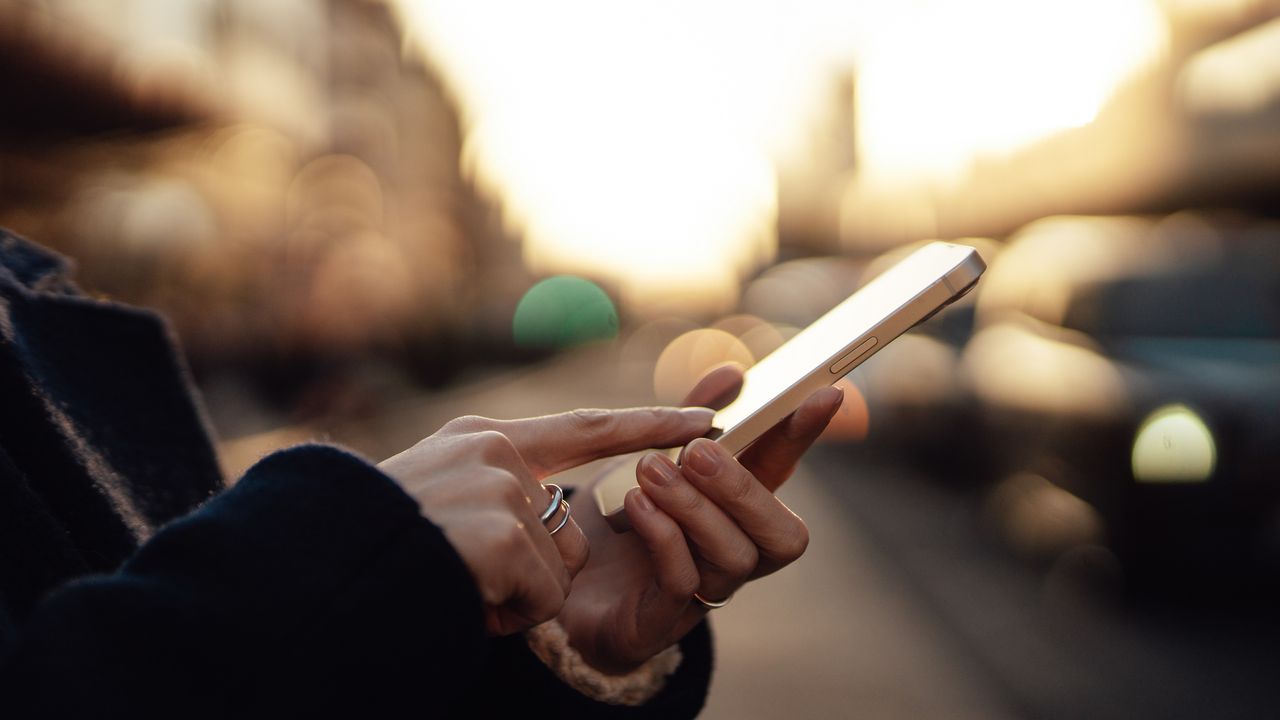 A woman uses her smartphone, a city&#039;s silhouette in the background.