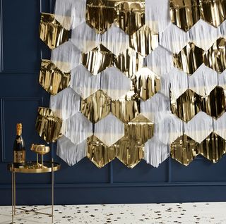dark blue wall decorated with gold and white foil fringe photo backdrop wine bottle and glasses on golden table