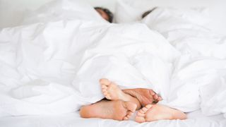 couple under the duvet cover in bed facing each other, with their feet at the end