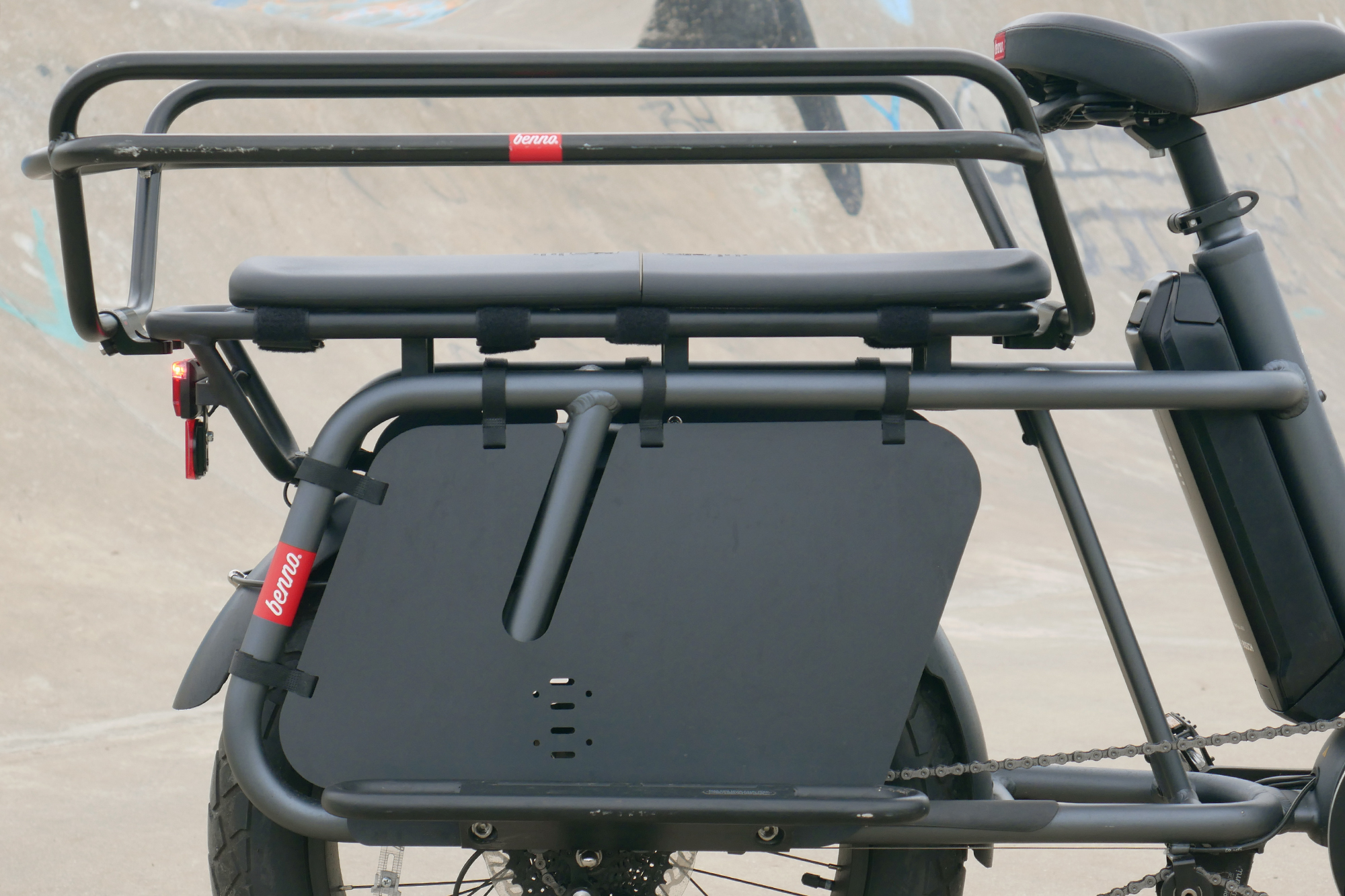 Rear passenger rack and rear wheel protection of the Benno RemiDemi XL against the backdrop of a concrete skatepark