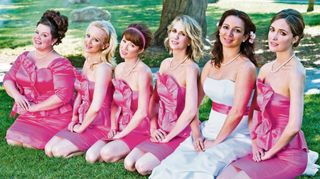 the cast of bridesmaids pose sitting down in their pink dresses and maia rudolph in her white wedding dress