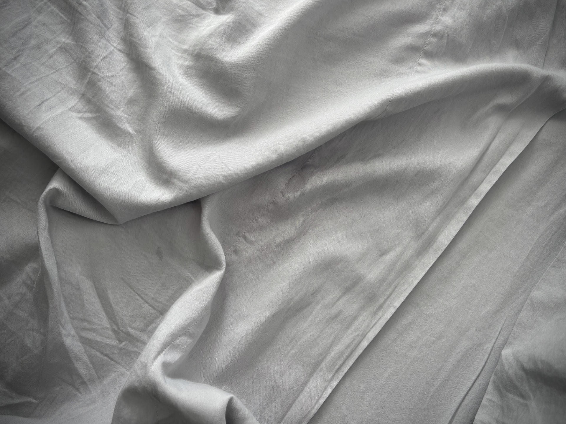 A wrinkled sheet lays atop a bed.
