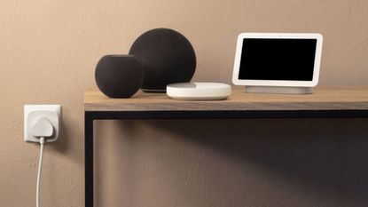 Lifestyle image of the Eve smart plug in the wall next to a table of Alexa devices