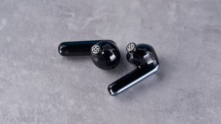 a pair of silver and black shiny earbuds with a black matte charging case are photographed against the Tom's Guide blue background