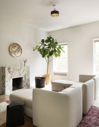 A living room with a large white couch, white walls and a tall plant